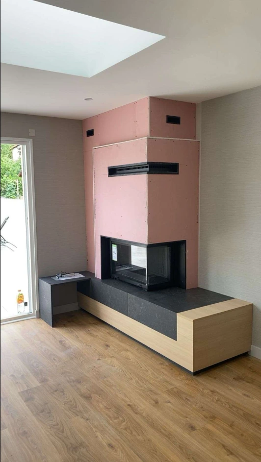 Cheminee d angle contemporaine avec foyer vitre double face, habillage rose et banc en bois clair et pierre noire